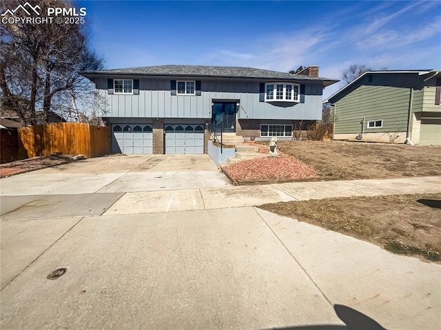 raised ranch with brick siding, concrete driveway, an attached garage, board and batten siding, and fence