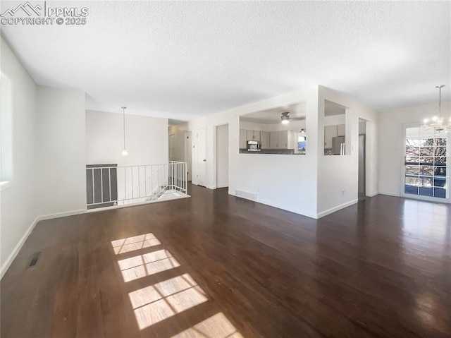 unfurnished living room featuring baseboards, visible vents, wood finished floors, a textured ceiling, and a chandelier