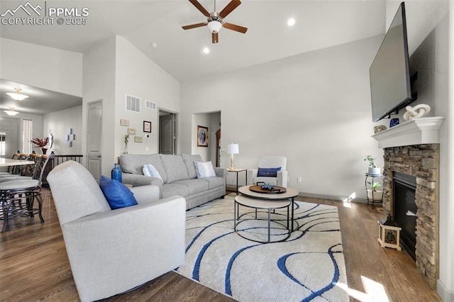 living area with a stone fireplace, wood finished floors, visible vents, and high vaulted ceiling