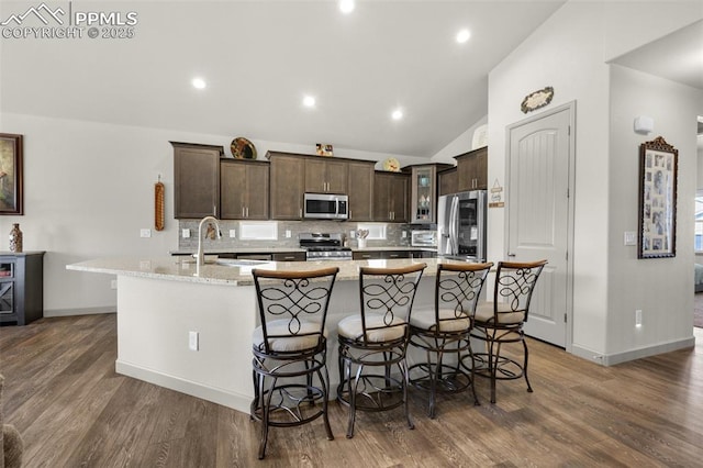 kitchen featuring dark brown cabinets, tasteful backsplash, appliances with stainless steel finishes, and a large island with sink