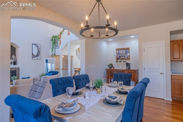 dining room with a notable chandelier, light wood-style flooring, stairs, and a tiled fireplace