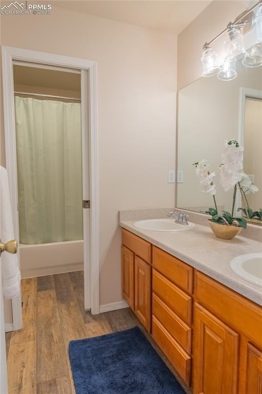 bathroom with shower / tub combo with curtain, double vanity, a sink, and wood finished floors