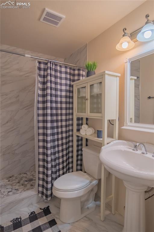 full bath with marble finish floor, visible vents, a tile shower, and toilet