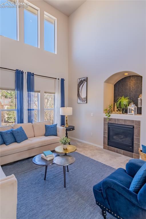 living room with carpet floors, baseboards, a towering ceiling, and a tiled fireplace