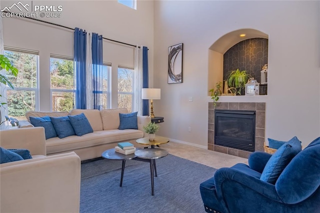 carpeted living area featuring a tile fireplace, a towering ceiling, and baseboards