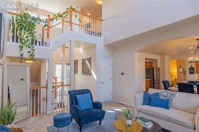 carpeted living room featuring baseboards, a high ceiling, arched walkways, and a notable chandelier