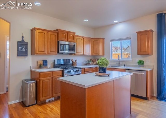 kitchen featuring stainless steel appliances, light wood finished floors, a sink, and light countertops