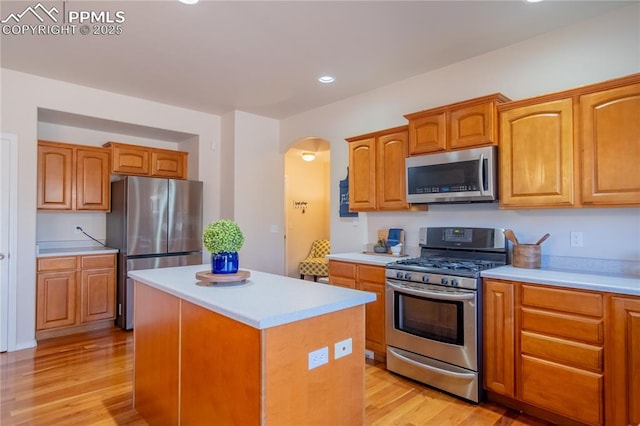 kitchen with appliances with stainless steel finishes, arched walkways, light countertops, and light wood-style flooring