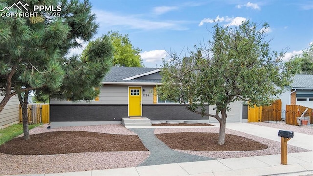 view of front of property featuring driveway, brick siding, an attached garage, and fence