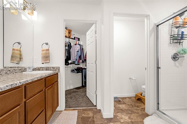 full bathroom with a walk in closet, toilet, a shower stall, vanity, and baseboards