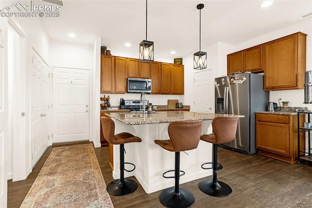 kitchen featuring dark wood-style floors, stainless steel appliances, brown cabinetry, a kitchen island with sink, and a sink