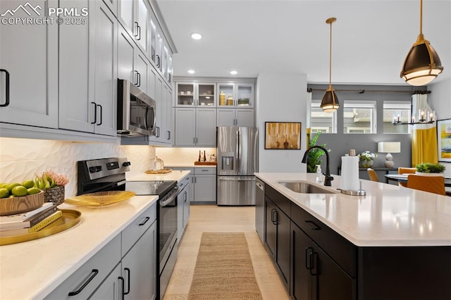 kitchen with decorative backsplash, an island with sink, appliances with stainless steel finishes, hanging light fixtures, and a sink