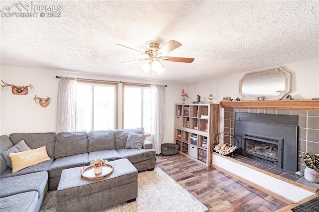 living room featuring a tiled fireplace, a textured ceiling, a ceiling fan, and wood finished floors