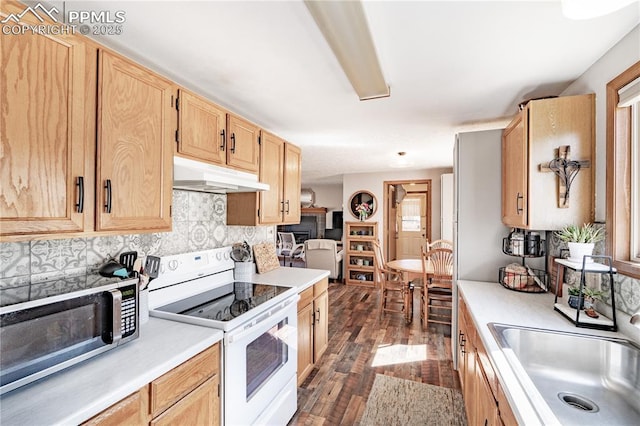 kitchen with light brown cabinets, under cabinet range hood, a sink, white electric range oven, and light countertops