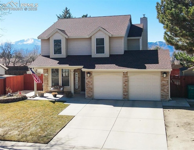 traditional home with a front yard, fence, brick siding, concrete driveway, and a mountain view