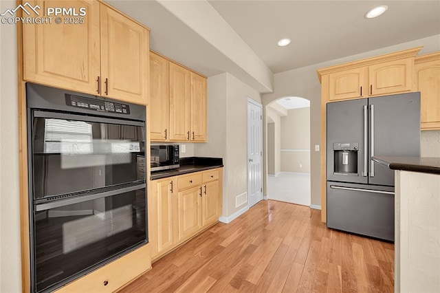 kitchen featuring arched walkways, light wood-style flooring, appliances with stainless steel finishes, light brown cabinetry, and dark countertops