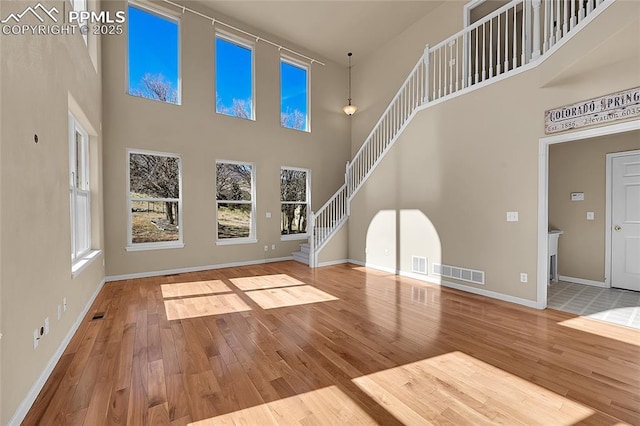 unfurnished living room featuring a wealth of natural light, wood-type flooring, visible vents, and stairway