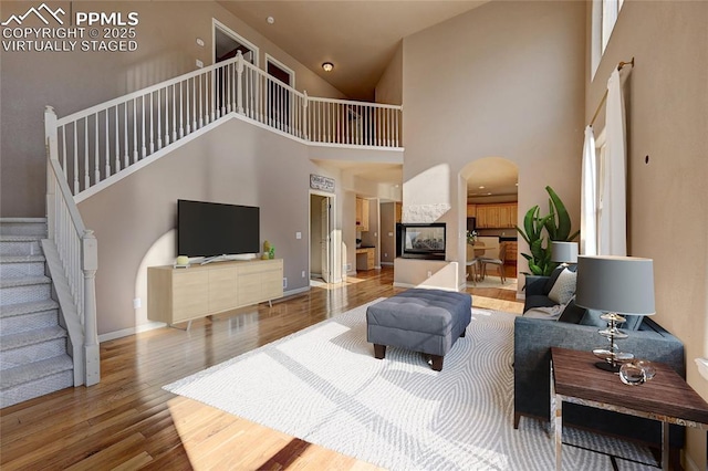 living room featuring arched walkways, a multi sided fireplace, wood finished floors, baseboards, and stairway