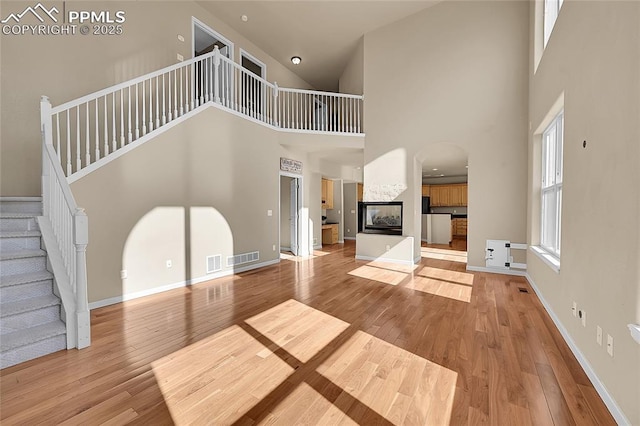 unfurnished living room with visible vents, hardwood / wood-style floors, a multi sided fireplace, baseboards, and stairs