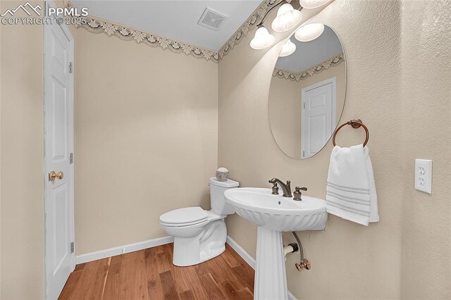 half bath featuring baseboards, visible vents, toilet, wood finished floors, and a sink