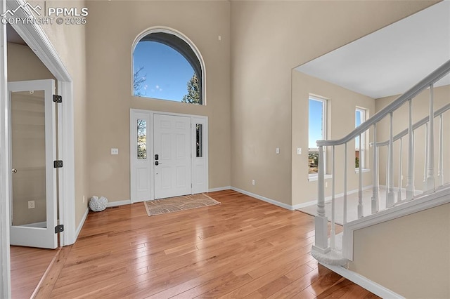 foyer with baseboards, a high ceiling, light wood finished floors, and stairs