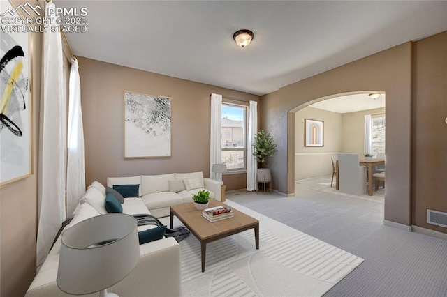 carpeted living room with a healthy amount of sunlight, baseboards, visible vents, and arched walkways