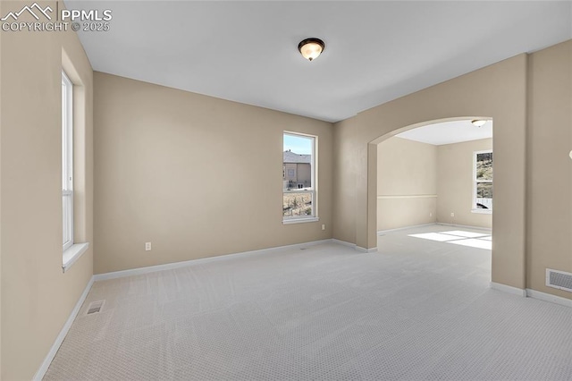 carpeted spare room with arched walkways, visible vents, and baseboards