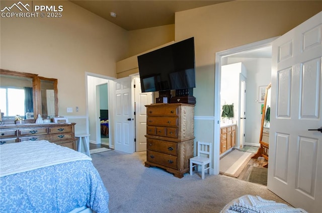 carpeted bedroom featuring ensuite bath and a high ceiling