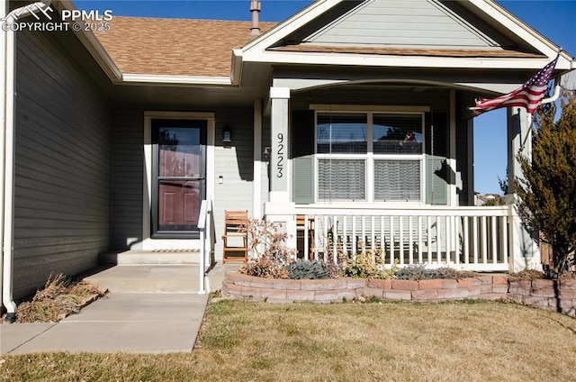 doorway to property with a porch, a lawn, and roof with shingles