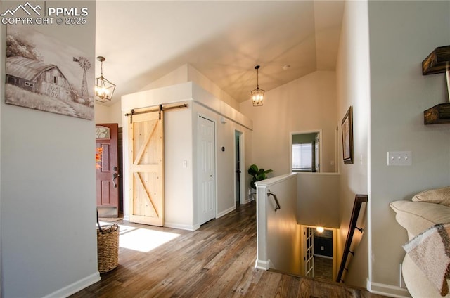 hallway featuring wood finished floors, baseboards, vaulted ceiling, a barn door, and an upstairs landing