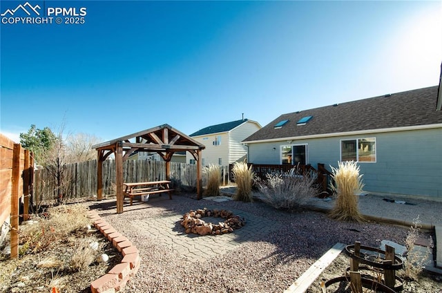 rear view of property featuring a fire pit, a shingled roof, a gazebo, a fenced backyard, and a patio area