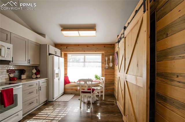 kitchen featuring dark wood finished floors, light countertops, a barn door, decorative backsplash, and white appliances