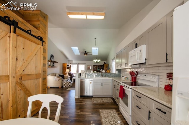 kitchen featuring a sink, a barn door, white appliances, vaulted ceiling with skylight, and a peninsula