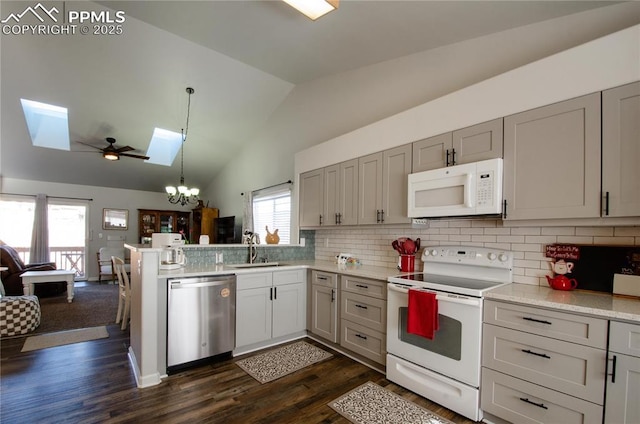 kitchen with open floor plan, vaulted ceiling with skylight, a peninsula, white appliances, and a sink