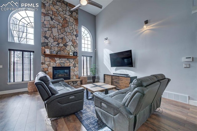 living room with high vaulted ceiling, a stone fireplace, plenty of natural light, and wood finished floors