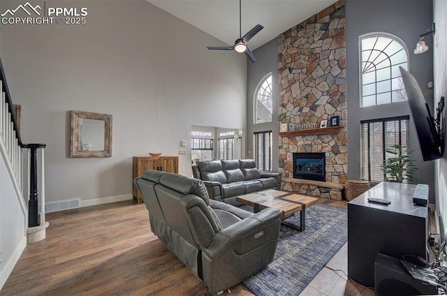 living room with a fireplace, visible vents, a ceiling fan, wood finished floors, and stairs