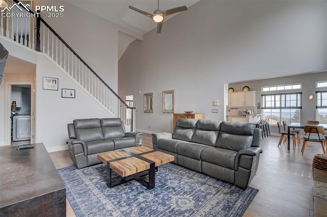 living room featuring a high ceiling, a ceiling fan, baseboards, stairway, and dark wood-style floors