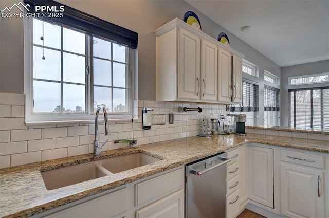 kitchen with light stone counters, a sink, white cabinets, stainless steel dishwasher, and backsplash