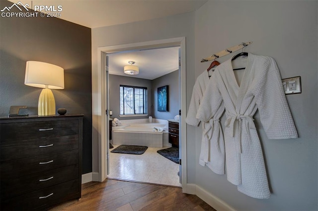 full bath with baseboards, a bath, and wood finished floors