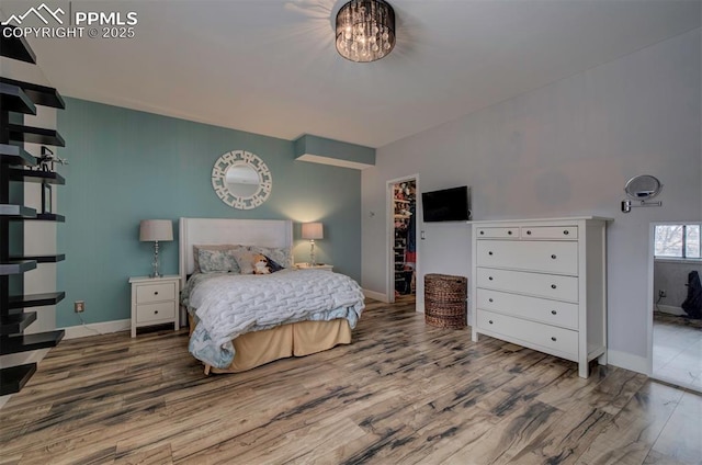 bedroom with a notable chandelier, wood finished floors, a walk in closet, and baseboards