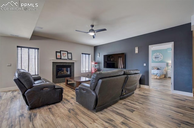 living room featuring visible vents, a tiled fireplace, ceiling fan, wood finished floors, and baseboards