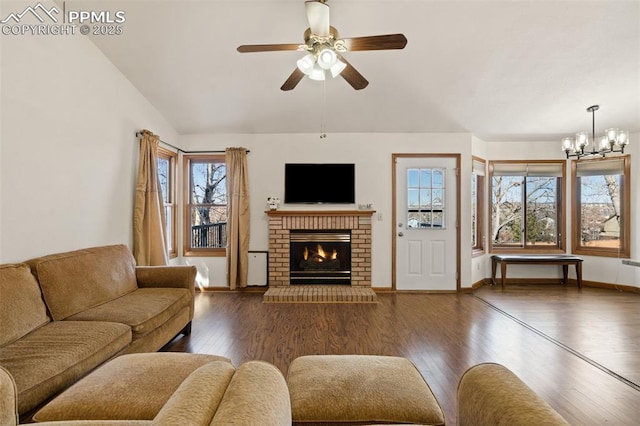 living room featuring ceiling fan with notable chandelier, vaulted ceiling, a fireplace, and wood finished floors