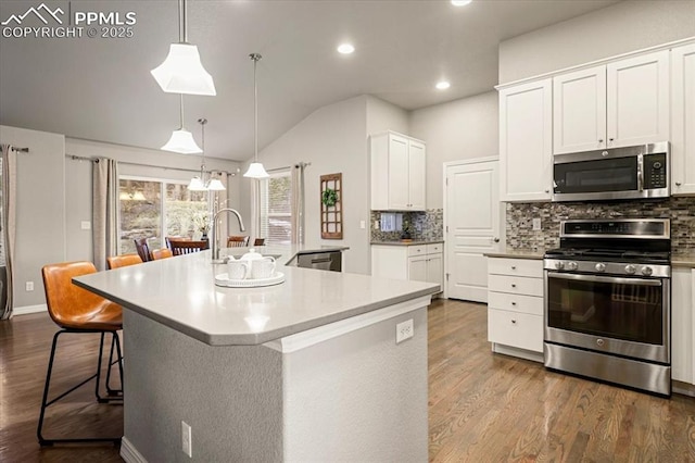 kitchen with dark wood-type flooring, a breakfast bar area, decorative backsplash, appliances with stainless steel finishes, and white cabinetry