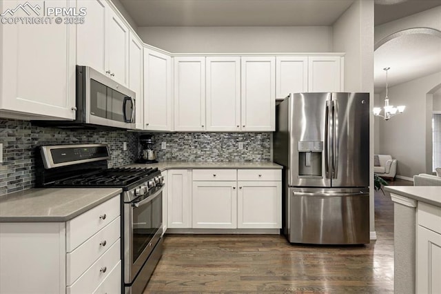 kitchen featuring backsplash, white cabinetry, stainless steel appliances, arched walkways, and dark wood-style flooring