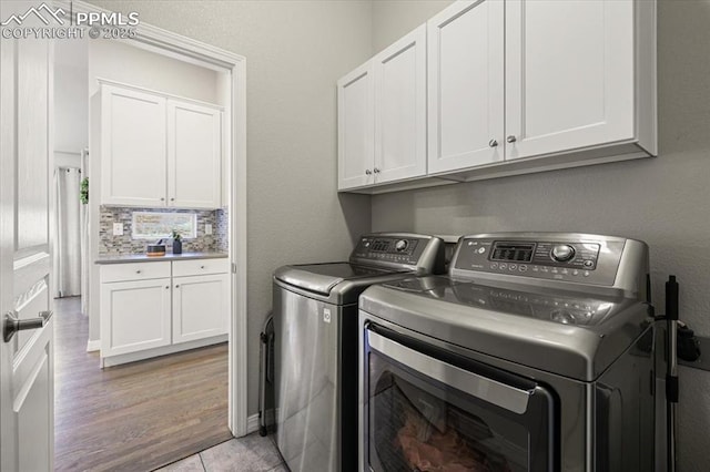 clothes washing area featuring cabinet space, light wood-style flooring, and washing machine and dryer