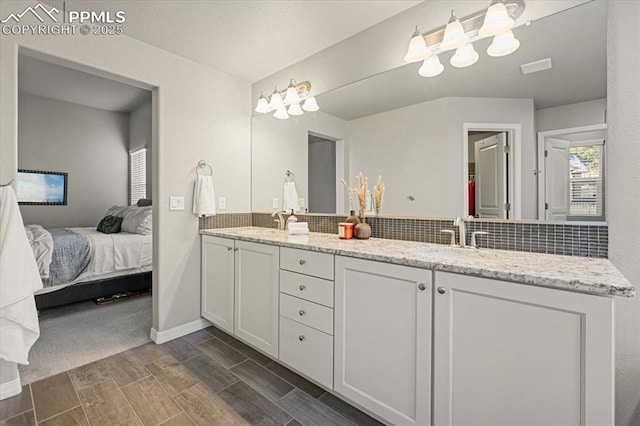 ensuite bathroom featuring wood tiled floor, double vanity, a sink, decorative backsplash, and ensuite bathroom