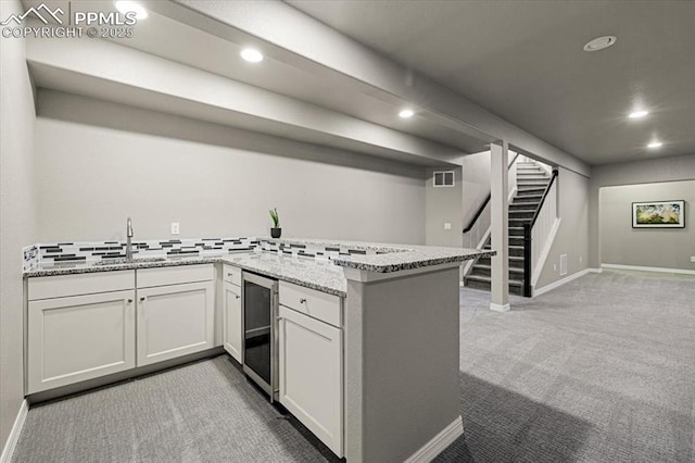 kitchen with visible vents, wine cooler, carpet floors, light stone counters, and a peninsula