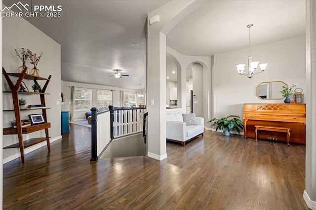 interior space featuring ceiling fan with notable chandelier, wood finished floors, arched walkways, and baseboards