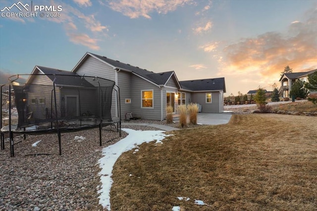 back of house at dusk featuring a yard, a trampoline, and a patio area