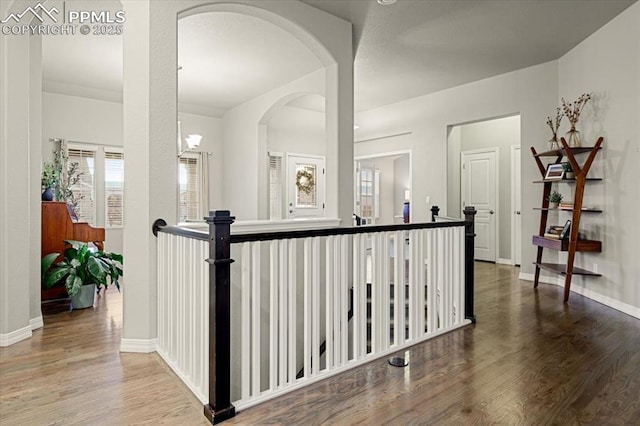 corridor with baseboards, arched walkways, and wood finished floors